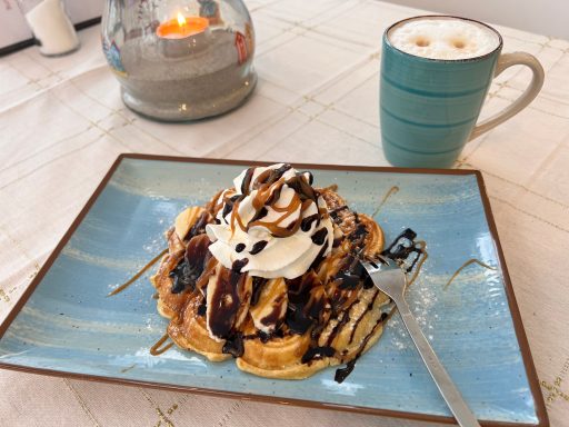 Waffeln mit Sahne, Schokoladensauce und einem Becher Latte auf einem Tisch.
