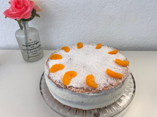 Käsekuchen mit Mandarinenstücken und Puderzucker, dekoriert mit einer rosa Rose im Hintergrund.