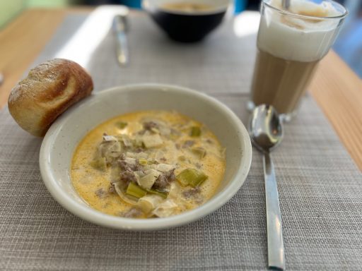 Schüssel mit cremigem Gericht, Brot und einem Glas Milchkaffee.
