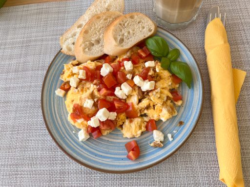 Rührei mit Tomaten und Feta, serviert mit Brot und frischen Basilikumblättern.